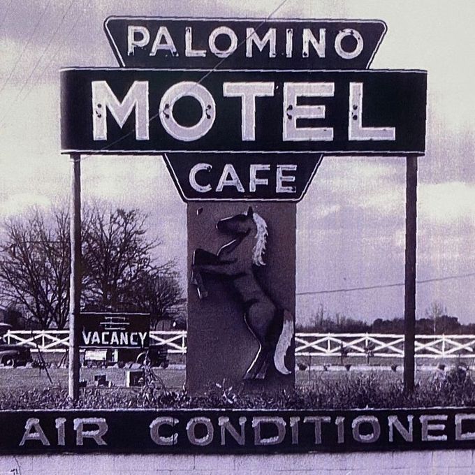Vintage Palomino Motel sign with cafe, vacancy, and air conditioning on a roadside in black and white.