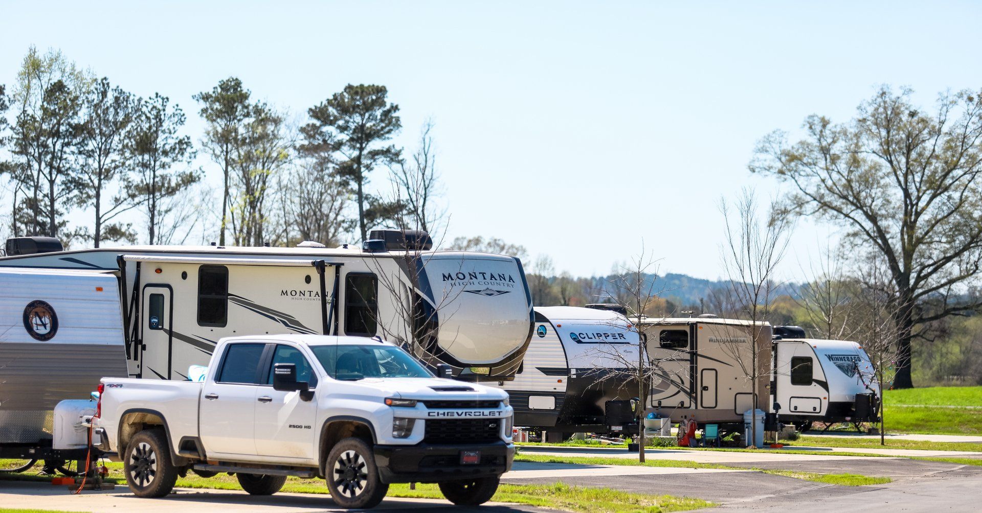 White pickup truck and RVs parked at a campground on a sunny day.
