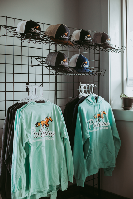Mint green shirts and hats displayed on a wire rack in a bright shop corner