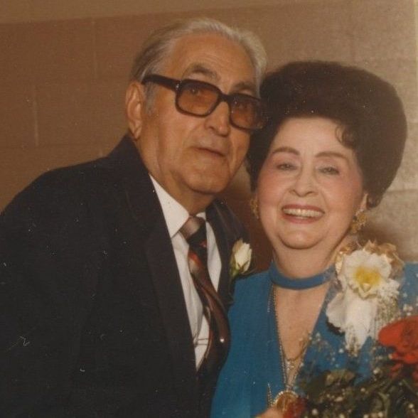 Smiling couple posing together at a formal event, with the woman holding flowers.