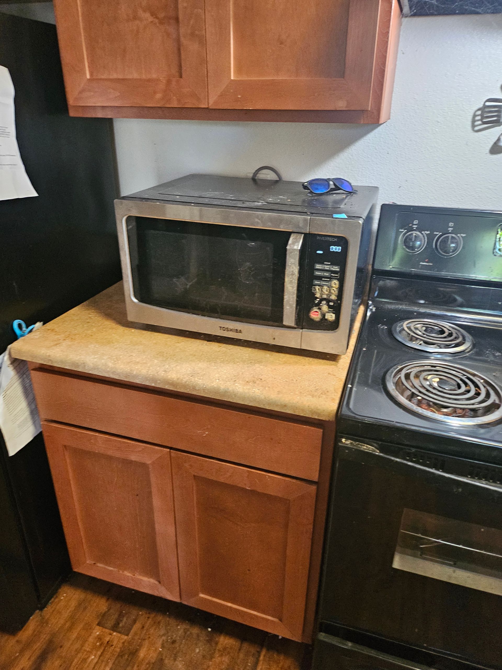 Microwave on beige kitchen counter beside a black stove and wooden cabinets