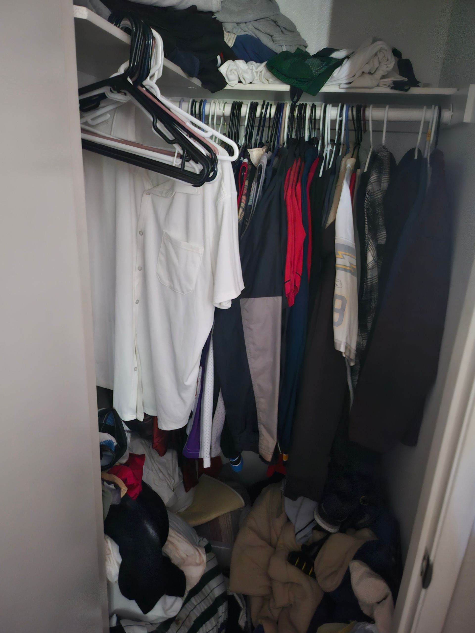 Open closet packed with hanging clothes, shoes, and a pile of items on the floor.