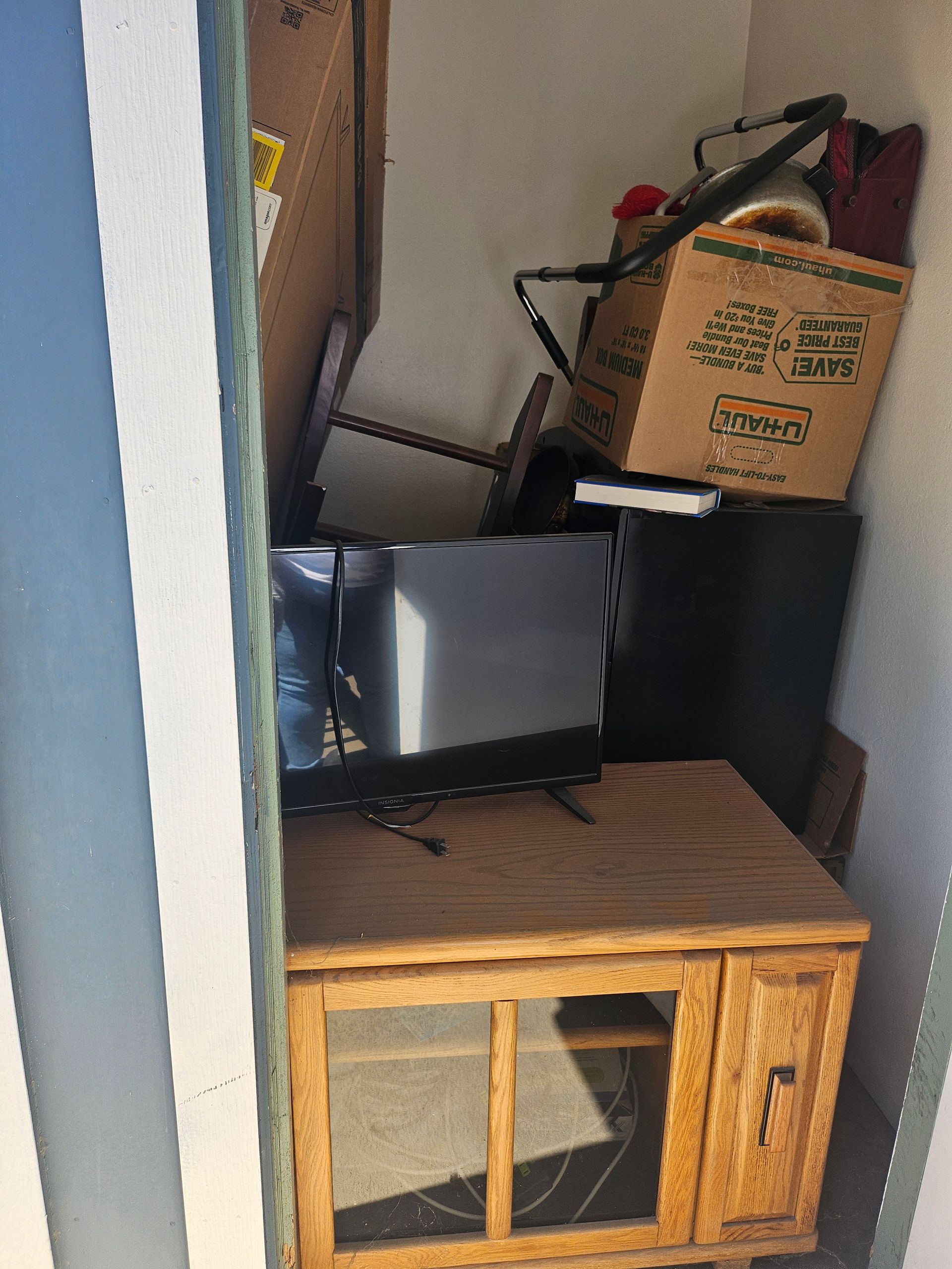 Small storage nook with a wooden cabinet, TV on top, and assorted boxes and tools stacked above.