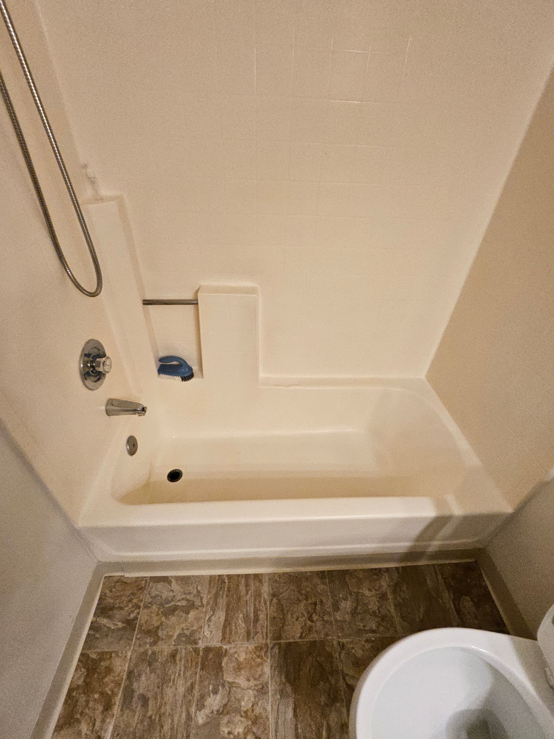 Small bathroom with white tub-shower, wall grab bar, and wood-look floor next to a toilet.