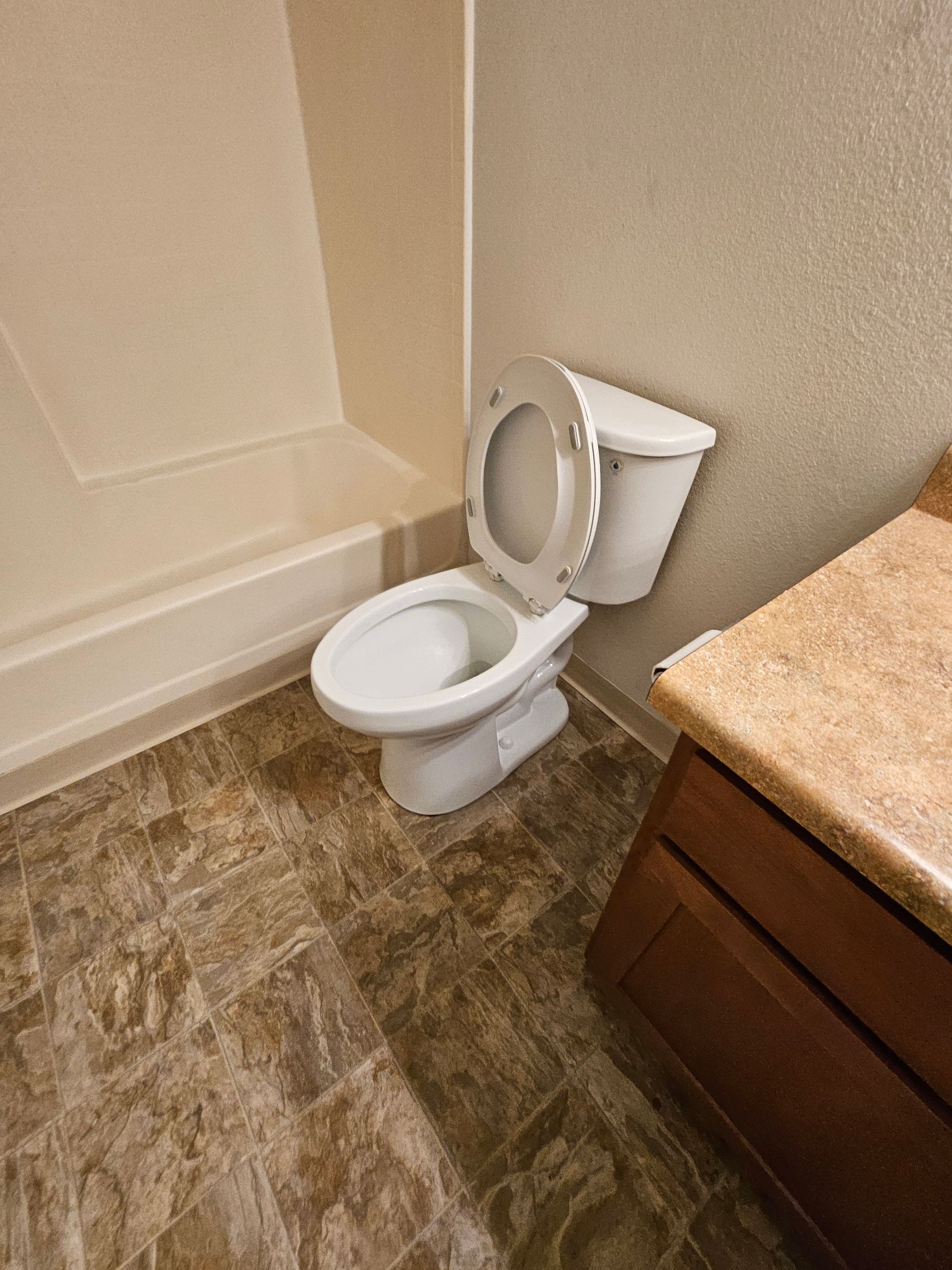 Small bathroom with an open toilet beside a beige tub and wood vanity.
