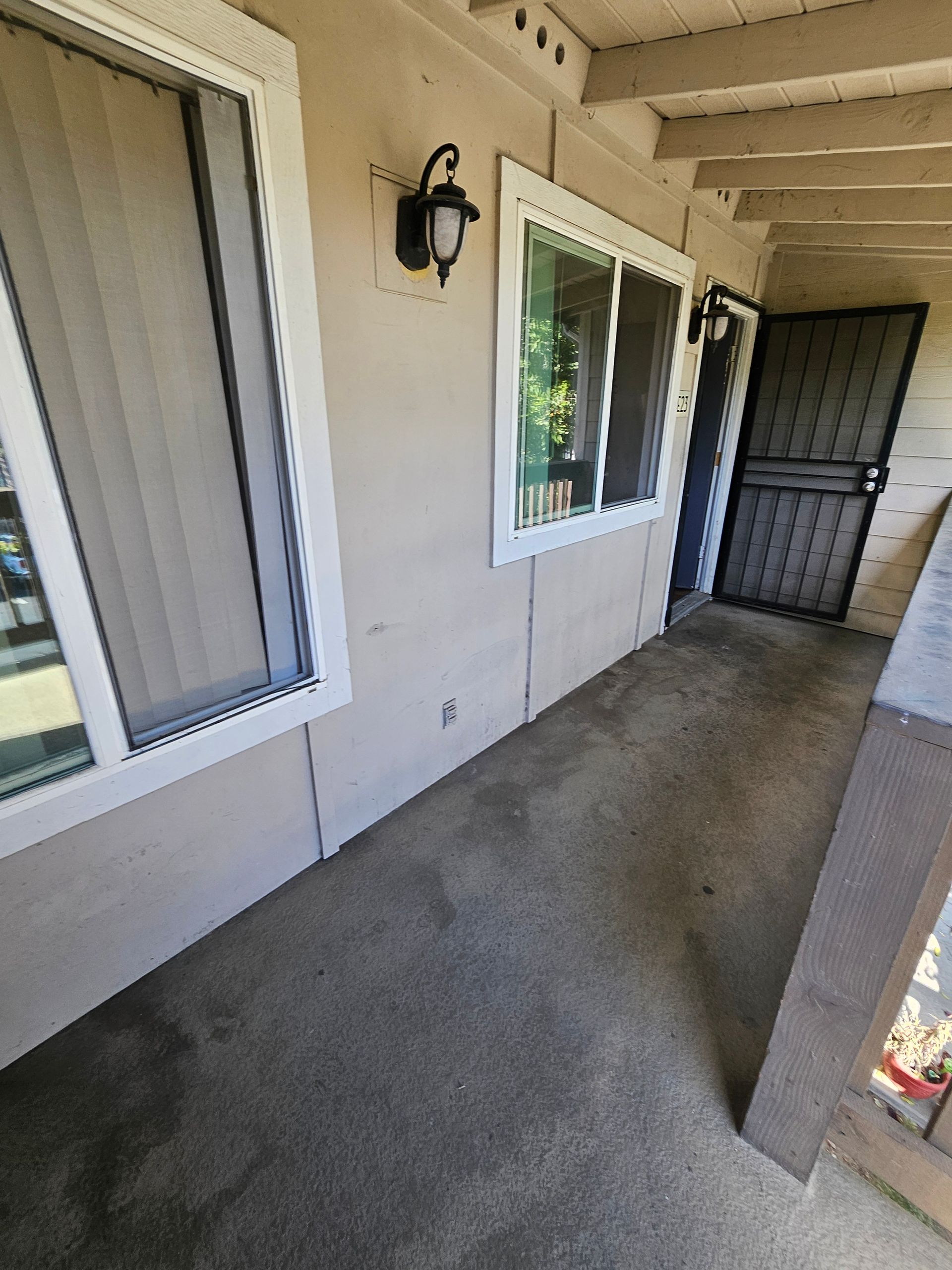 Covered apartment walkway with windows, door, wall light, and concrete floor.