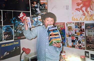 A boy is holding a stack of books in a room with posters on the wall that say scalextric