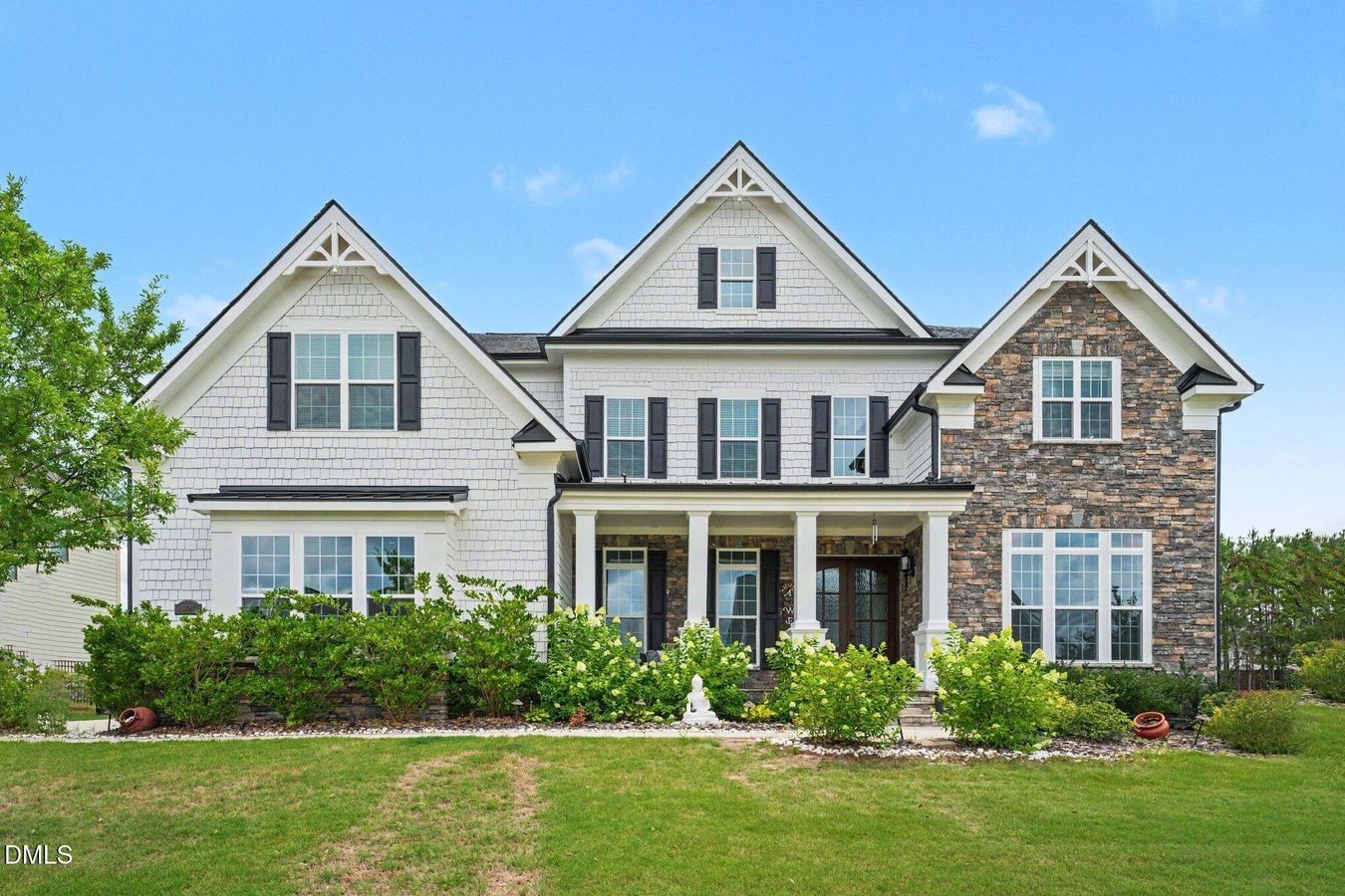 Large white suburban house with stone accents, front porch, and landscaped lawn under a blue sky