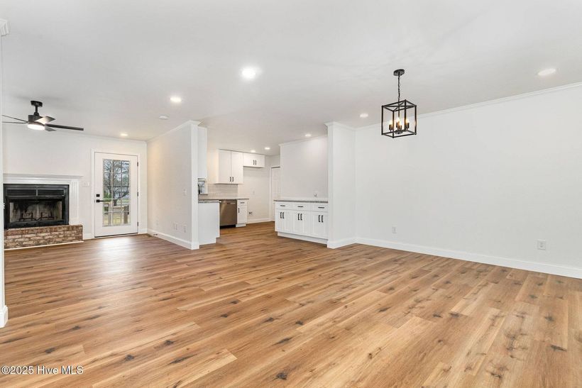 Spacious empty living room with hardwood floors, white walls, fireplace, and ceiling lights