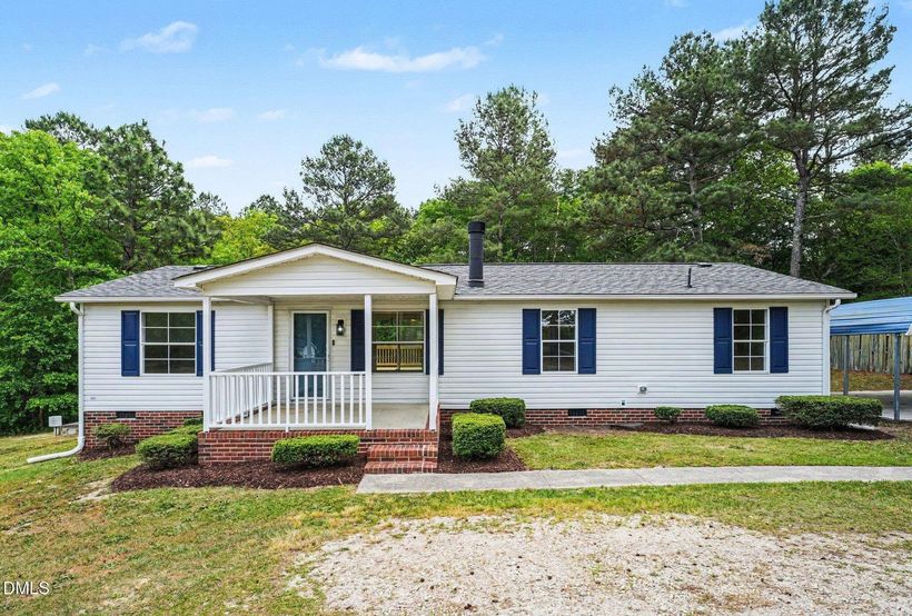 Single-story white house with blue shutters, small front porch, and grassy yard under trees