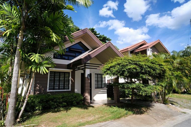 Single-story house with red roof, white trim, and palm trees in a sunny yard