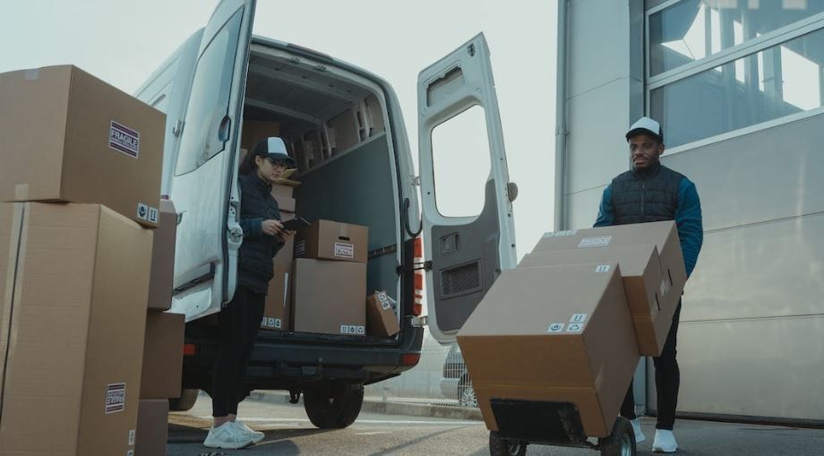 Workers unloading cardboard boxes from a delivery van outside a modern building.