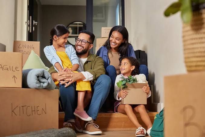 Family sitting among moving boxes in a sunlit living room, smiling and relaxed