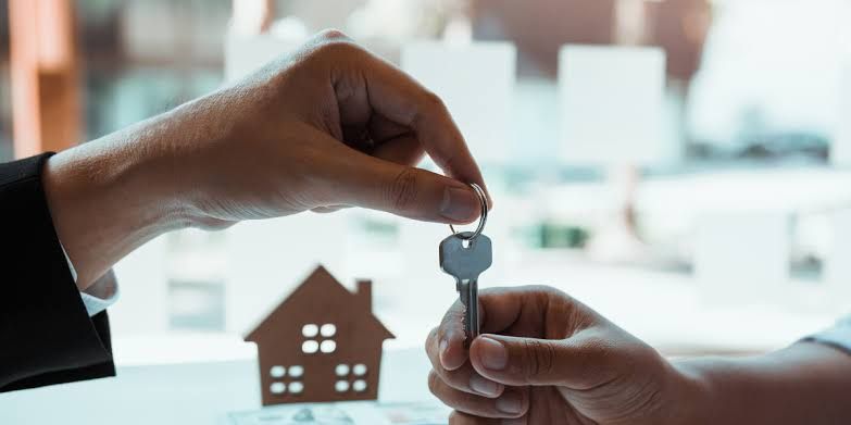Handing over a house key, with a small house icon in the foreground