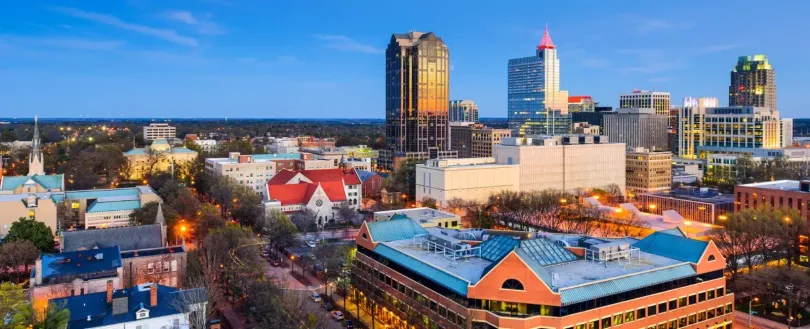 Downtown city skyline at dusk with lit high-rises and buildings under a blue sky