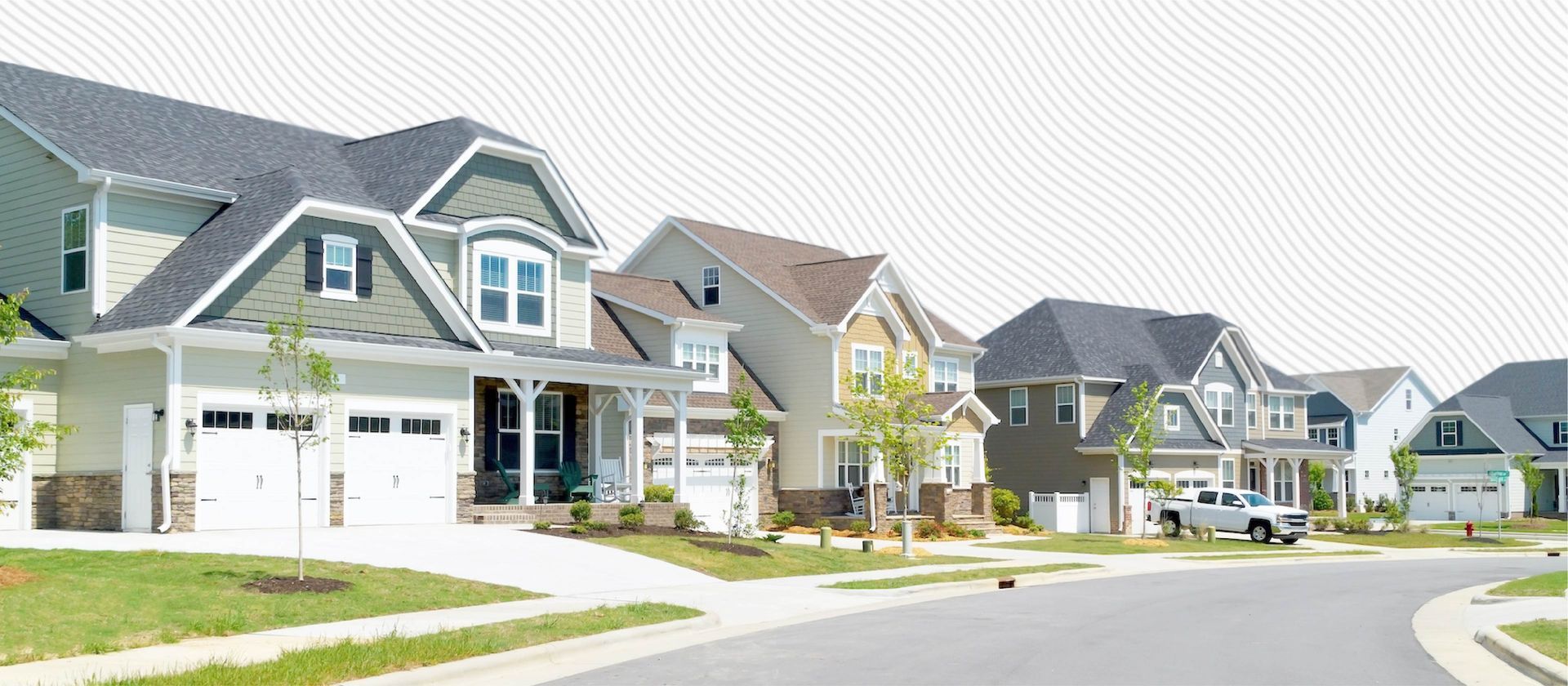Suburban street with rows of modern houses, green lawns, and a curved road on a bright day