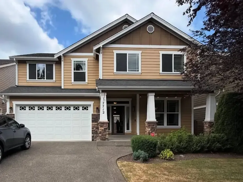 Two-story suburban house with tan siding, white garage, and front porch, viewed from the driveway