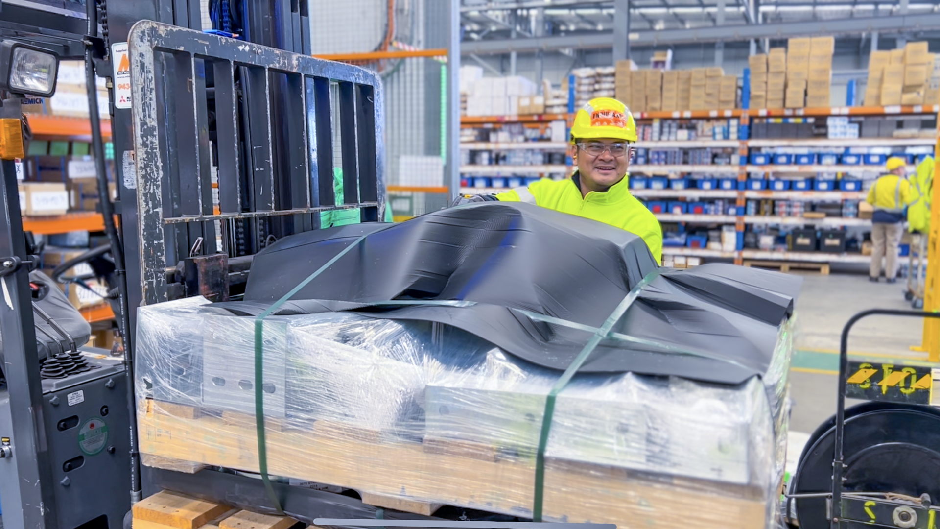 A warehouse worker wearing yellow hi-vis loading a forklift
