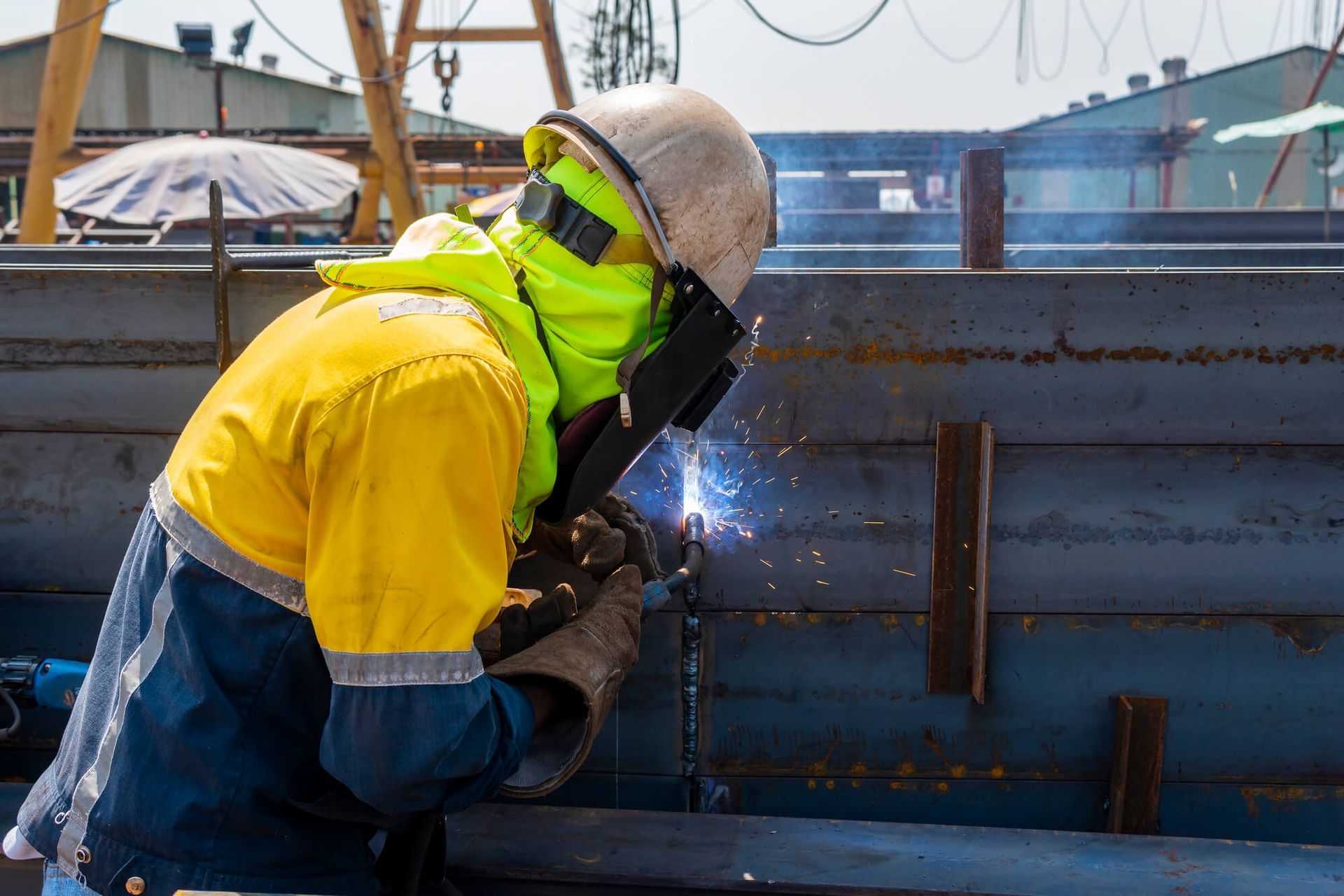 A welder wearing a yellow safety top and safety mask