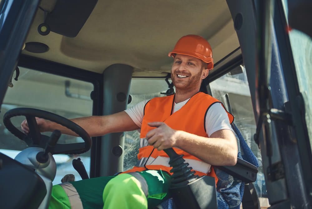 A truck driver wearing orange hi-vis and an orange hard hat driving a truck