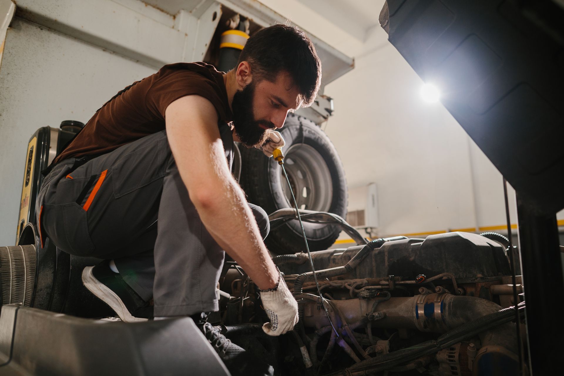 Mechanic working on a car engine in a garage; crouched down, using a tool.