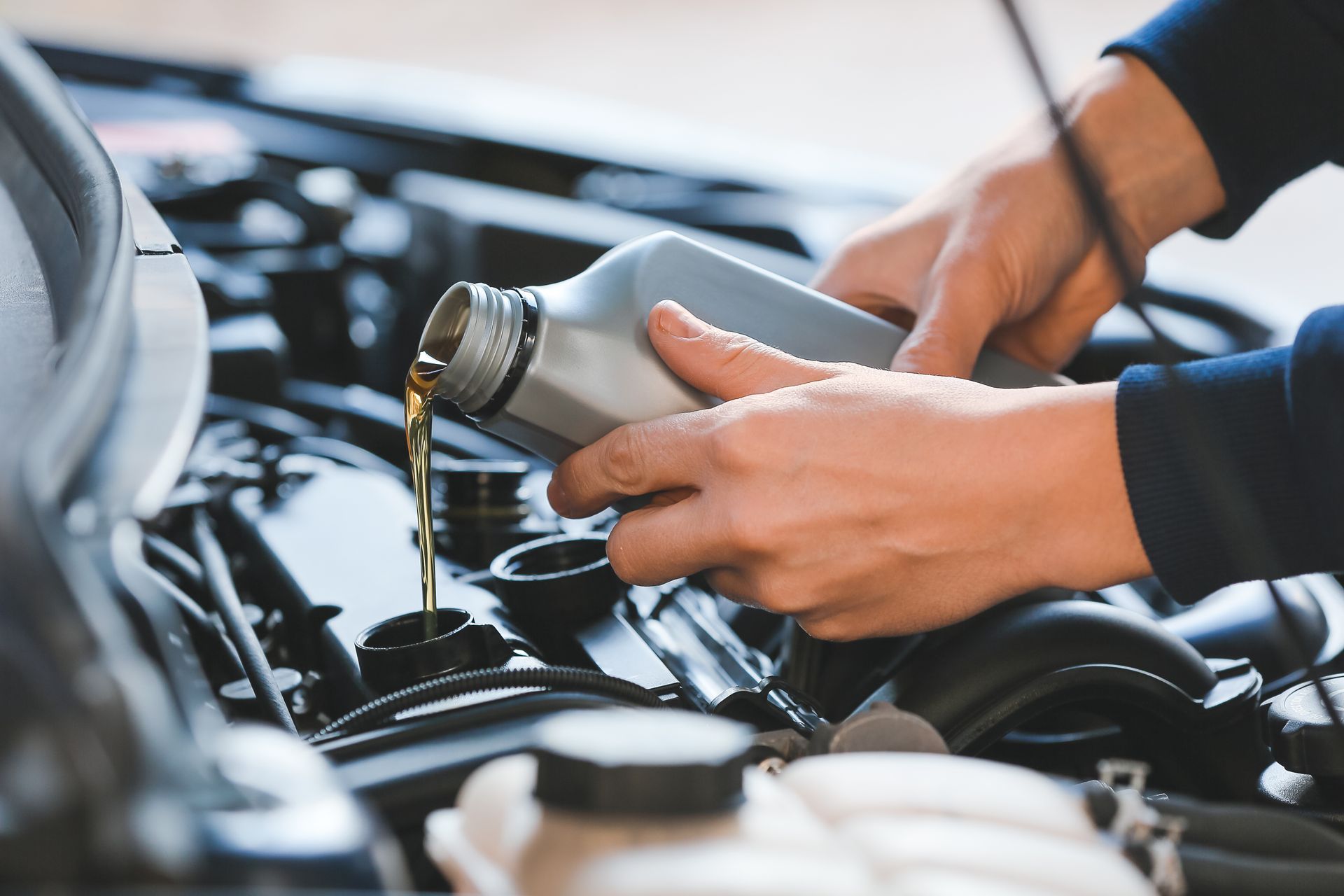 Hands pouring oil from a bottle into a car engine, in an open engine bay. Hands pouring oil from a bottle into a car engine, in an open engine bay.