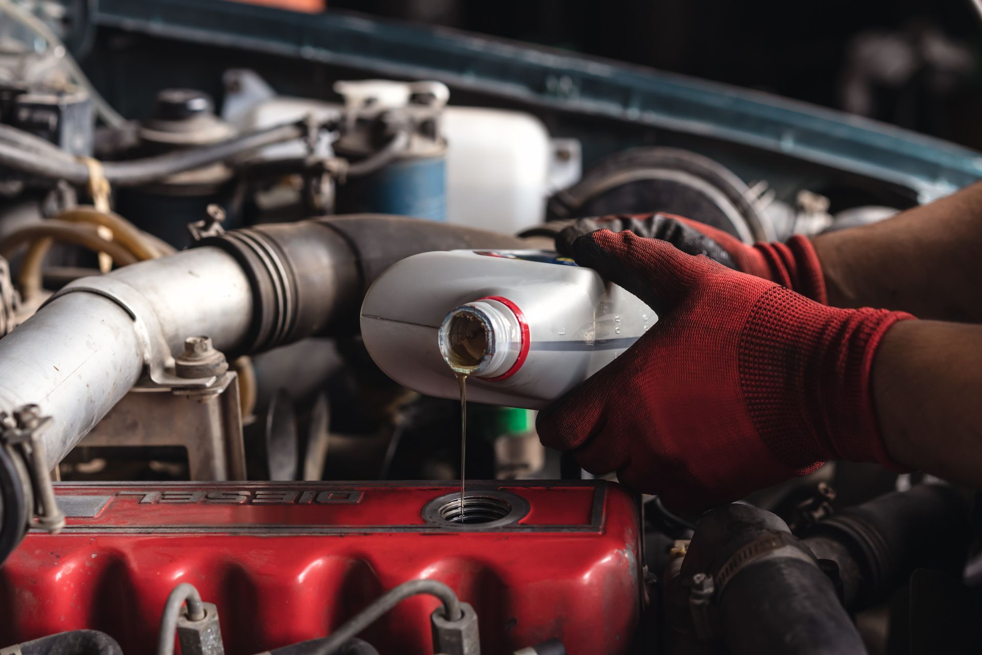 Mechanic pouring oil into a car engine, hands in red gloves.
