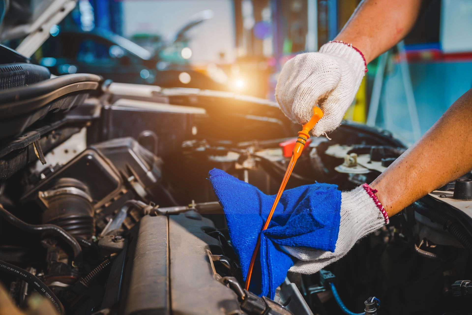Hands in gloves checking engine oil with a dipstick and blue cloth in a garage. Hands in gloves checking engine oil with a dipstick and blue cloth in a garage.
