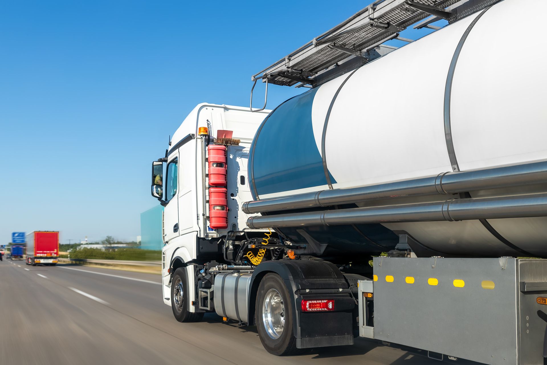White tanker truck driving on highway, blue sky.
