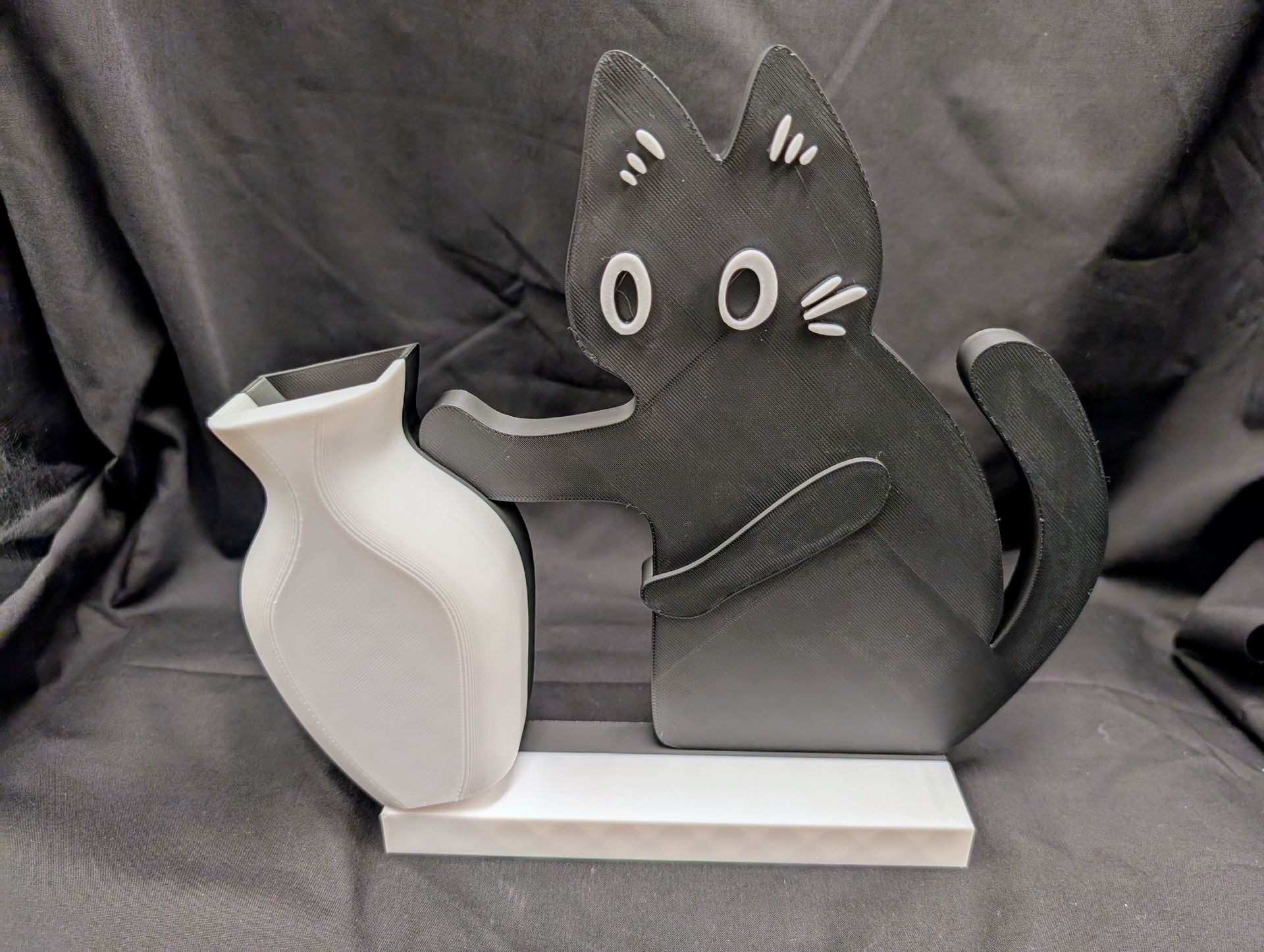 Big black cat model pushing over a small white vase.