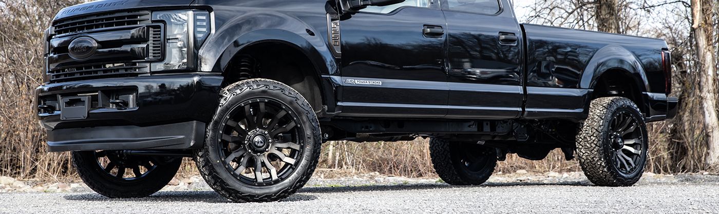 Black lifted pickup truck with tinted windows parked on gravel in a side view