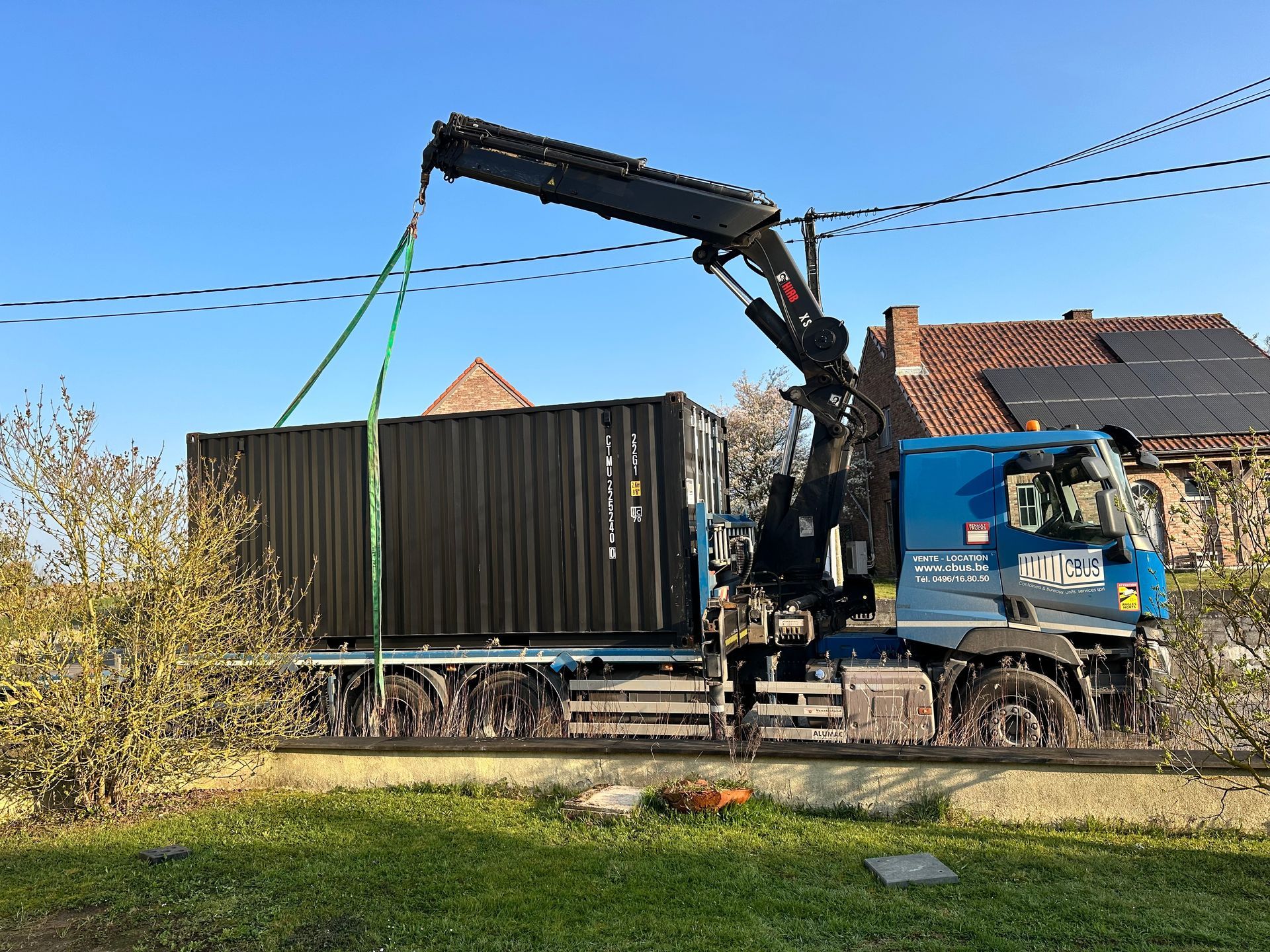 Camion-grue CBUS déposant un container maritime 20 pieds noir sur un terrain