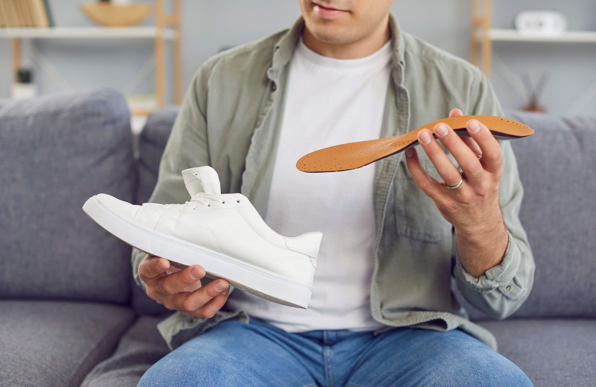 A man is sitting on a couch holding a pair of shoes and an insole.