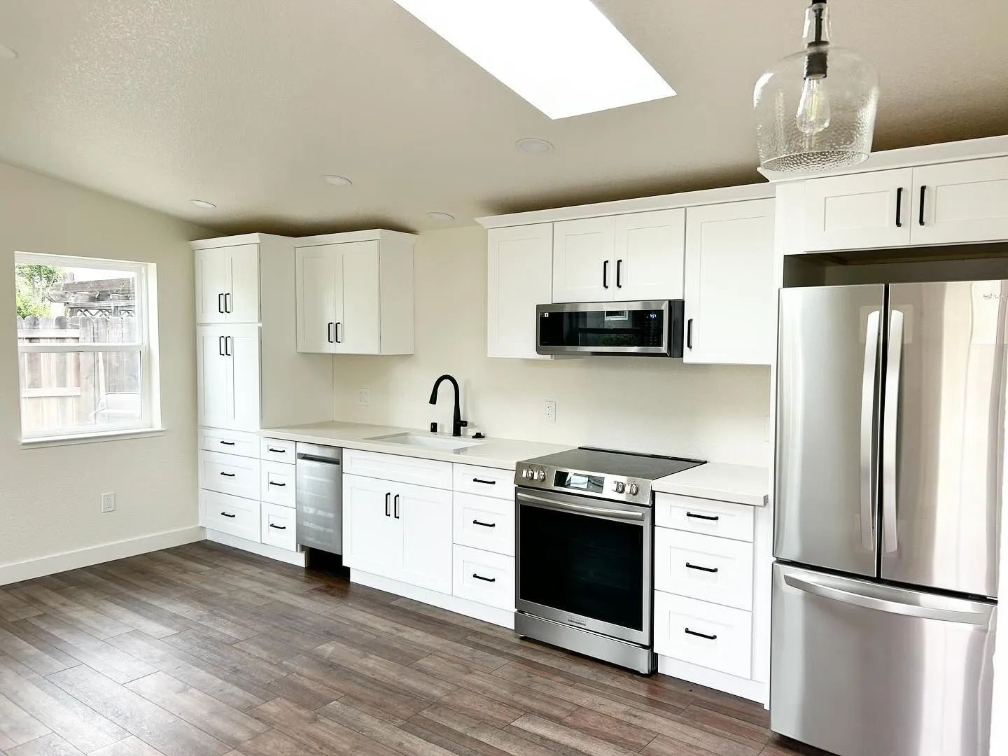 Bright white kitchen with stainless steel appliances, black countertops, and light wood floors