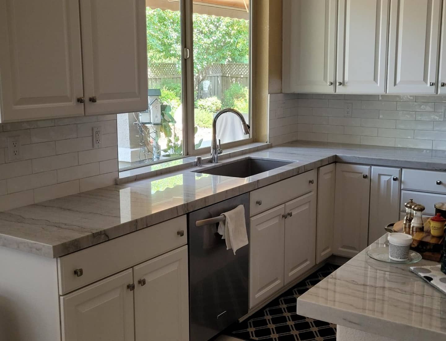 Bright kitchen with white cabinets, stone countertops, window over sink, and a small table with drinks.