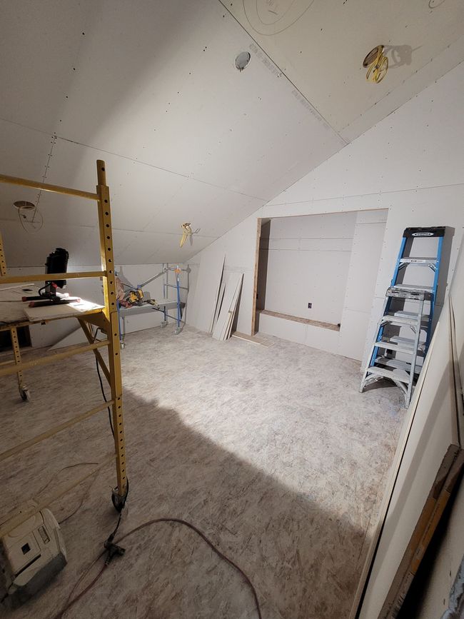 Unfinished attic room with scaffolding, a ladder, and white walls under renovation