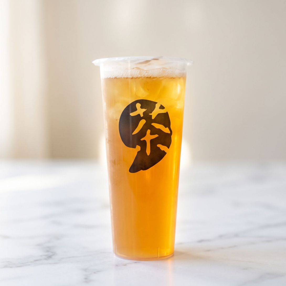 Clear plastic cup of amber iced drink with a black logo, standing on a white marble surface.