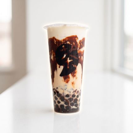 Tall clear cup of iced milk tea with chocolate drizzle and tapioca pearls on a bright white background