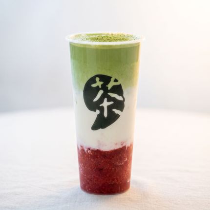 Tall clear cup of layered green, white, and red drink with a black tea logo on the front