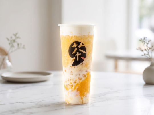 Tall clear cup with orange drink, whipped foam, and a black logo on a white table