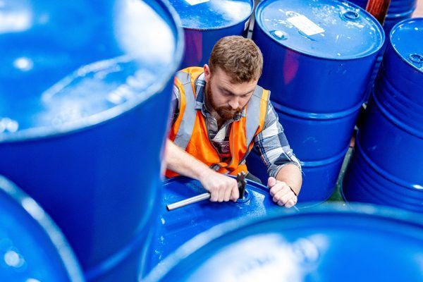 a man is working on a blue barrel in a warehouse .