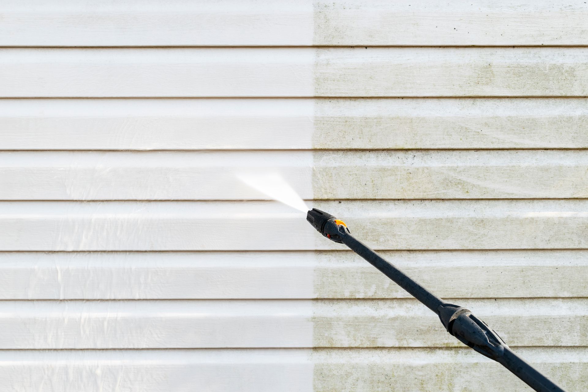 Pressure washer spraying a white vinyl siding wall, cleaning a dirty section