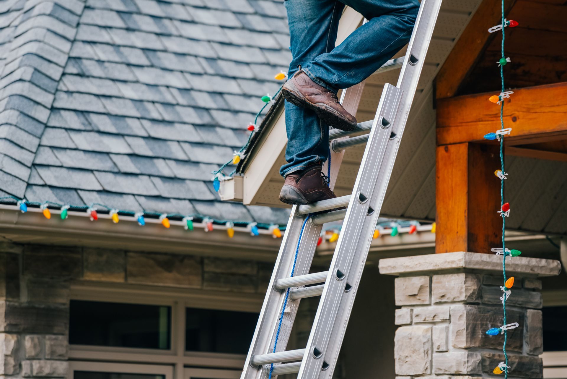 Person on ladder hanging Christmas lights on a house roofline