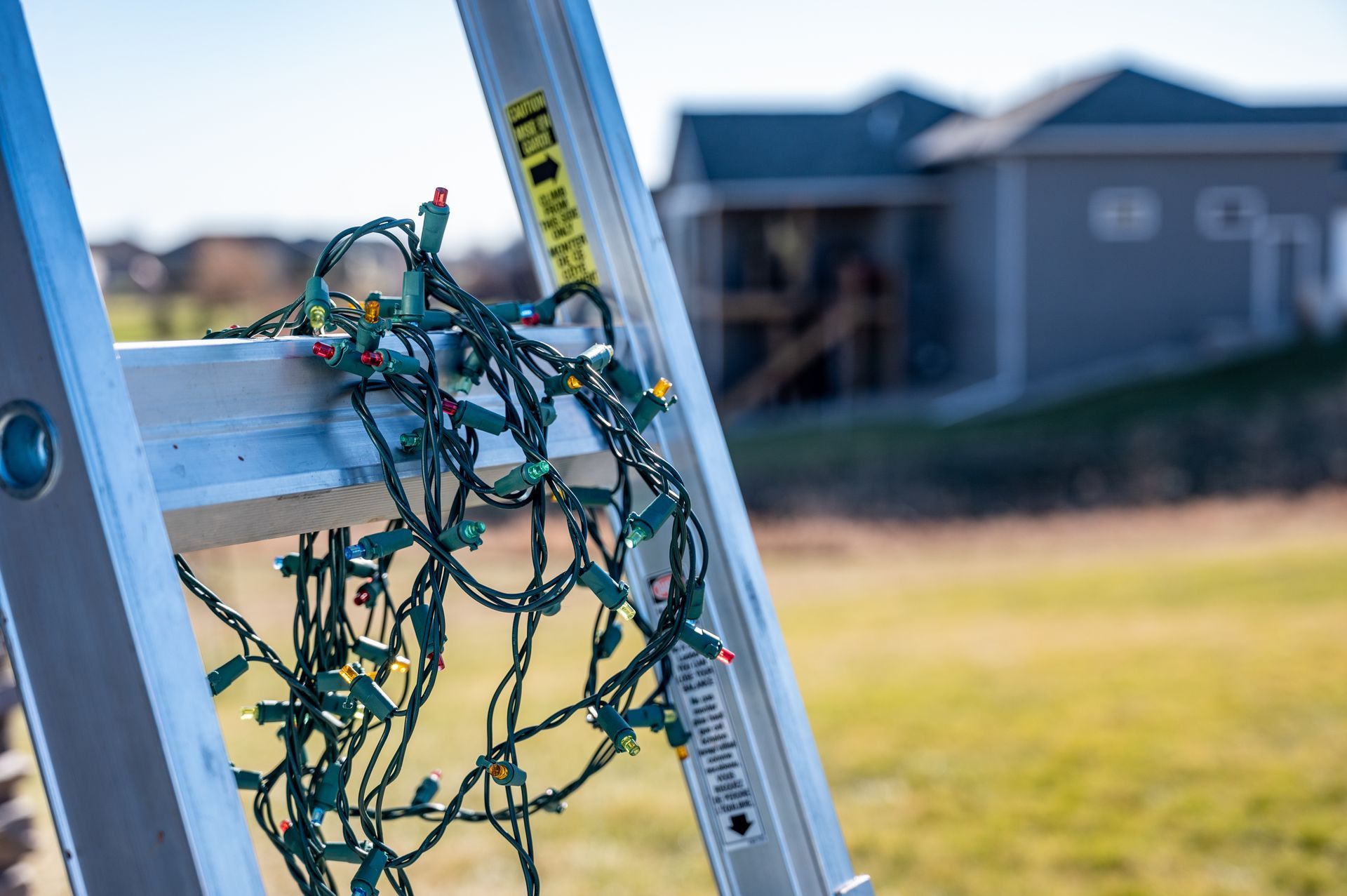String lights tangled on a ladder beside a house in a yard