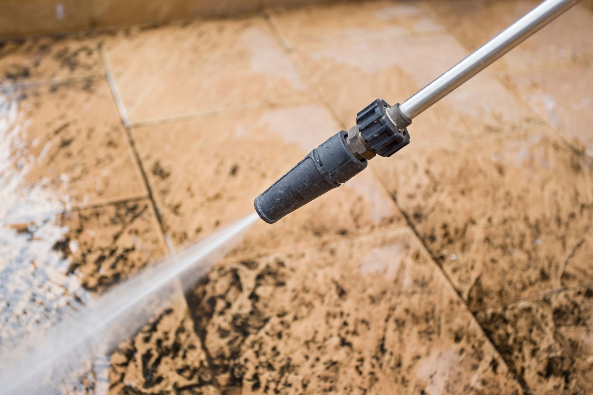 Pressure washer spraying water across a dirty tiled surface