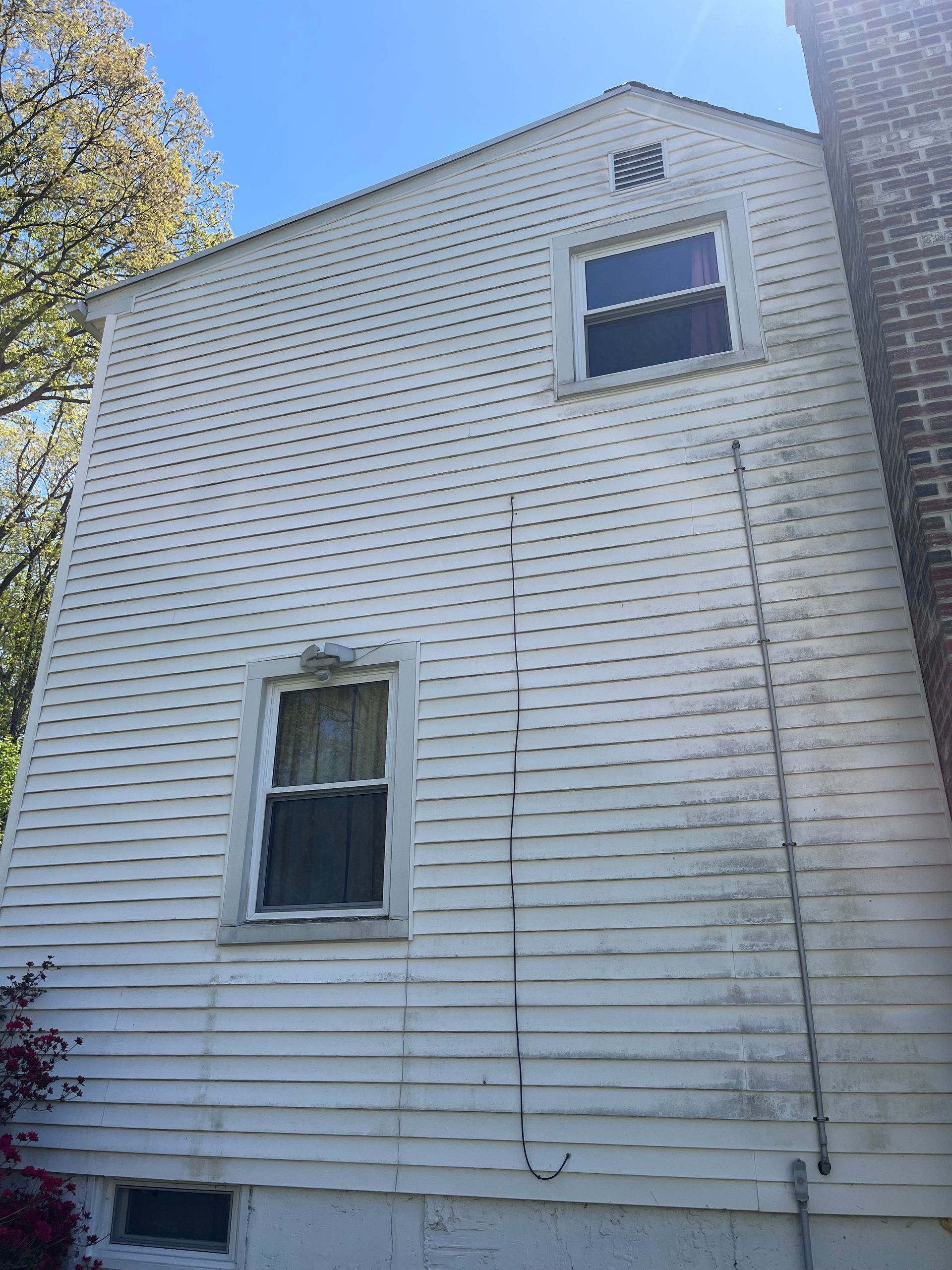 White clapboard house side wall with two windows and a brick chimney, seen from below against a blue sky