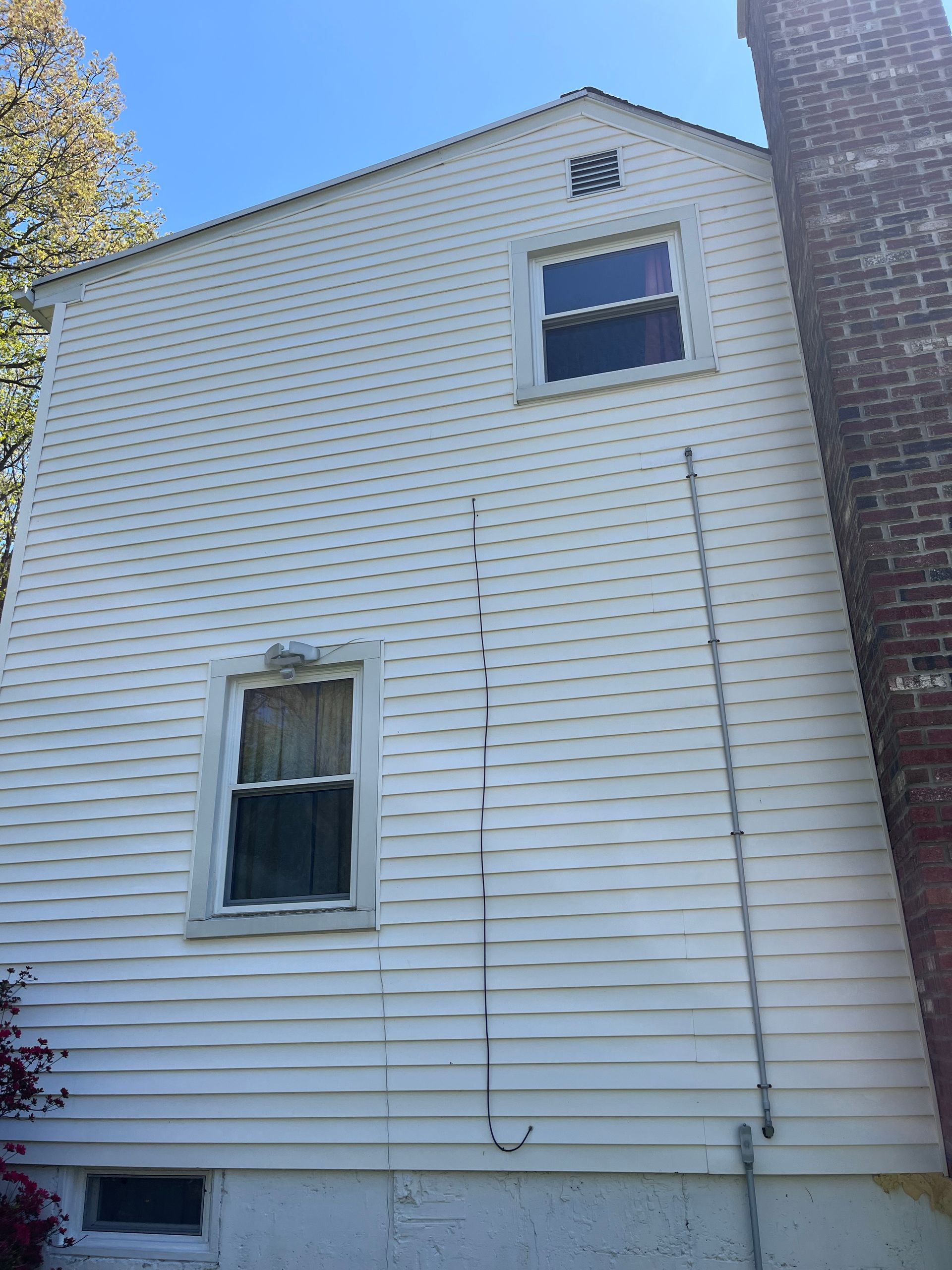 White house exterior with vinyl siding, two windows, and a brick corner under a blue sky