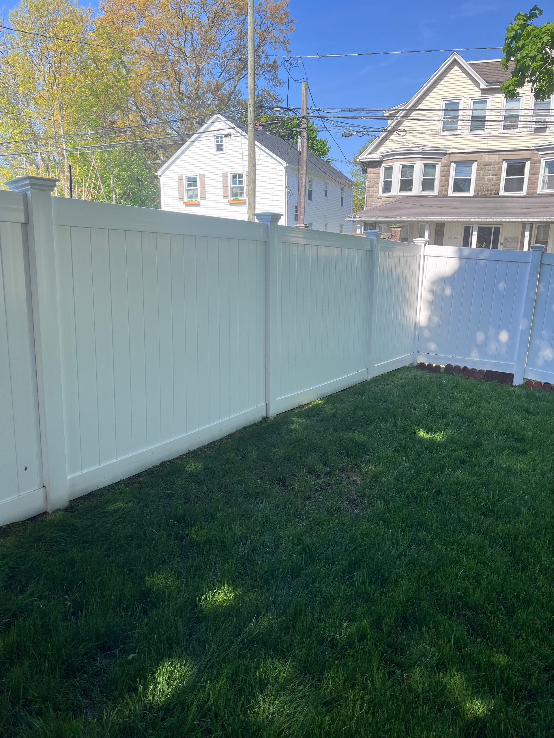 White vinyl fence bordering a green lawn with houses and autumn trees in the background