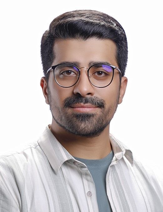 A person with a beard and glasses wears a light-colored striped shirt over a blue top, centered against a white background.
