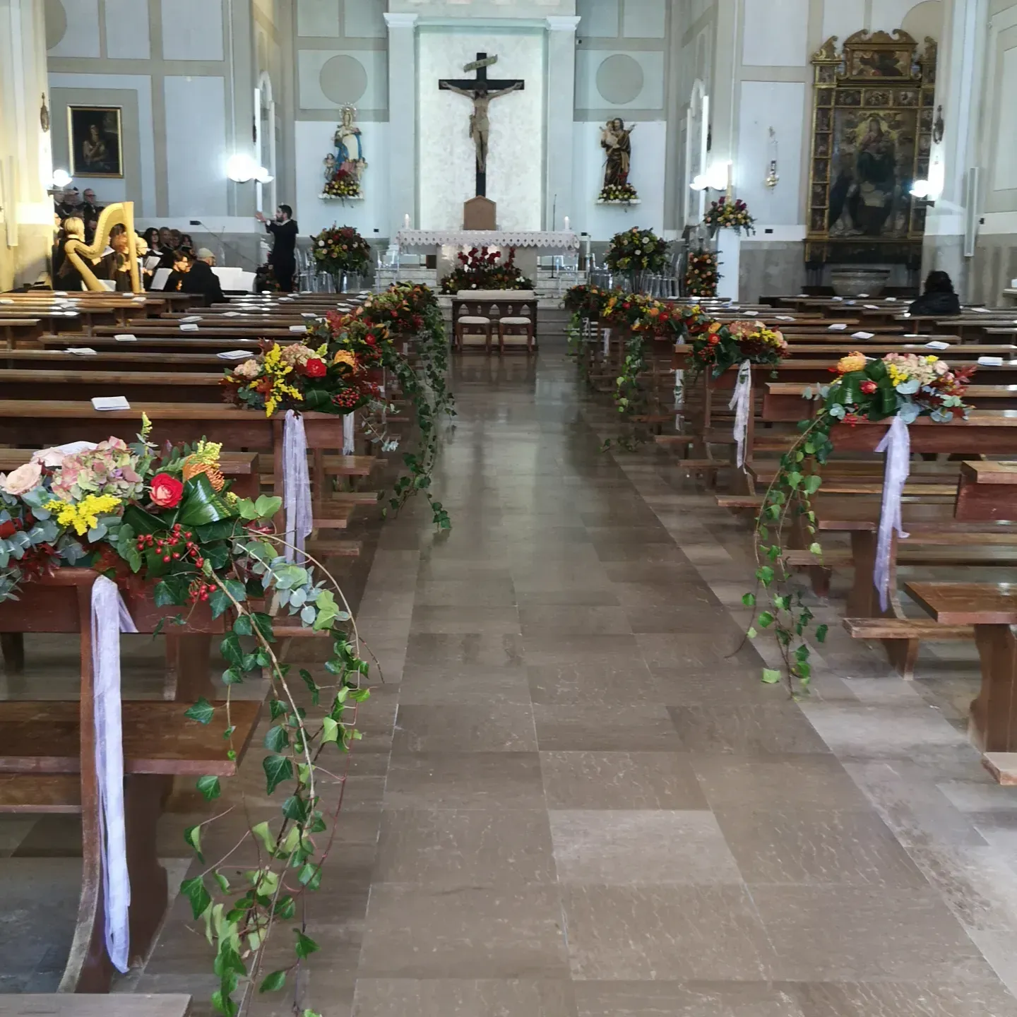 Vista interna della navata di una chiesa, decorata con composizioni floreali e nastri sui banchi che conducono all'altare.